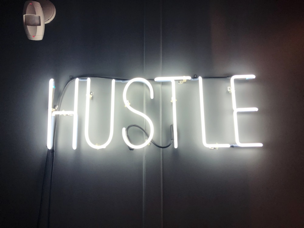 white neon sign reading 'hustle' in block font