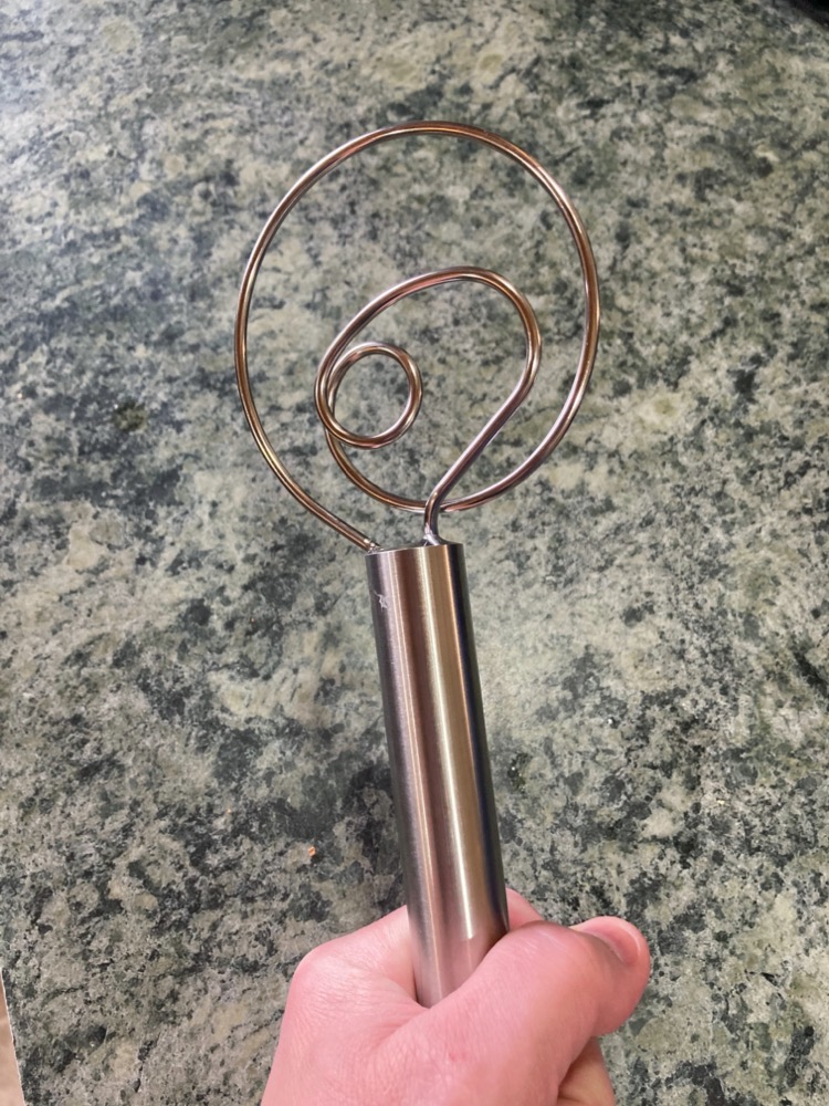 post author's hand holding up a bread whisk