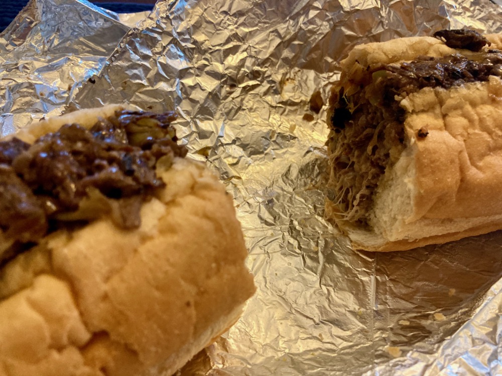 cheesesteak sandwich cut in half and sitting on foil