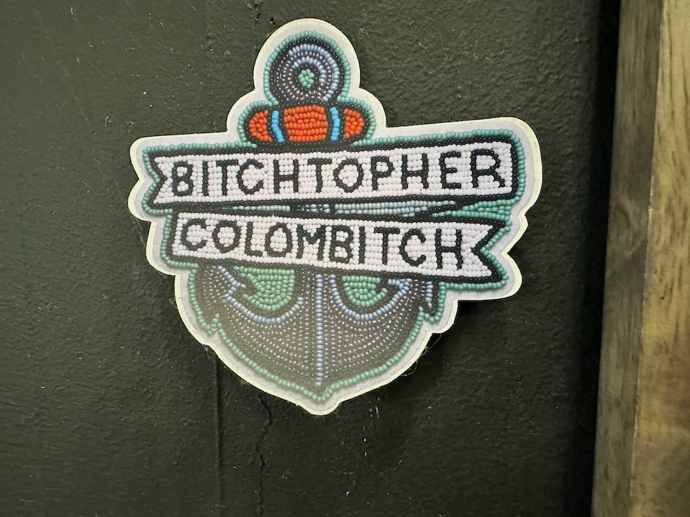 A sticker from the gym, with a faux-NatAm beading style anchor tattoo with an overlaid ribbon that reads BITCHTOPHER COLOMBITCH